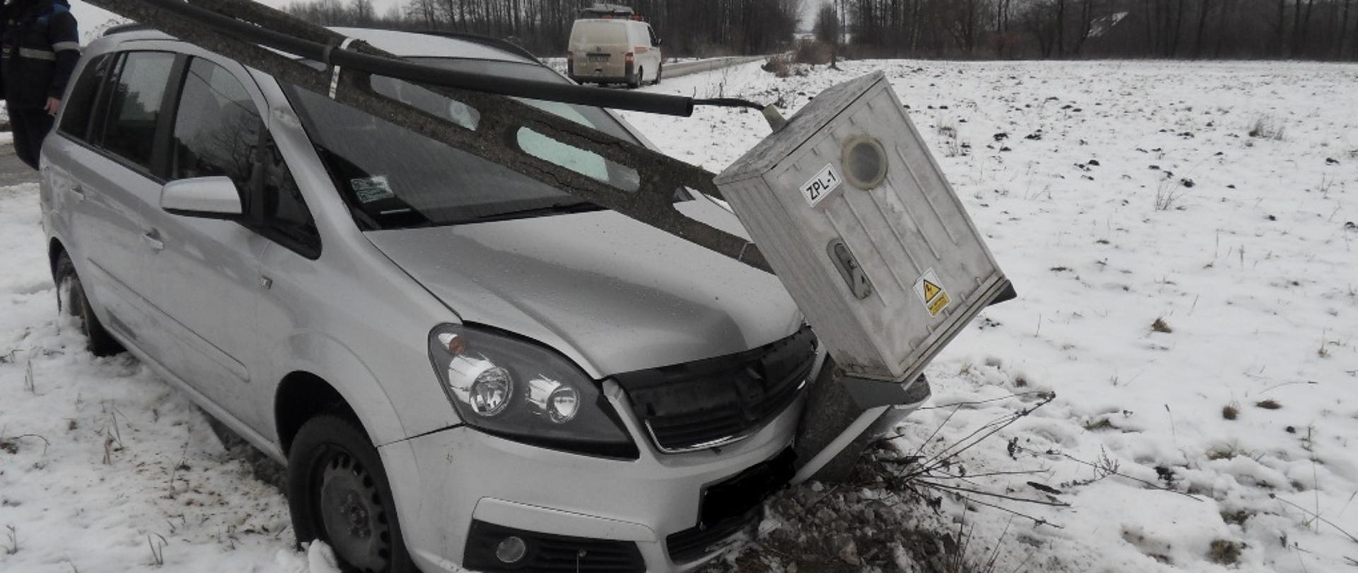 Uszkodzony o słup elektryczny przód samochodu osobowego oraz złamany słup elektryczny wiszący nad dachem pojazdu.