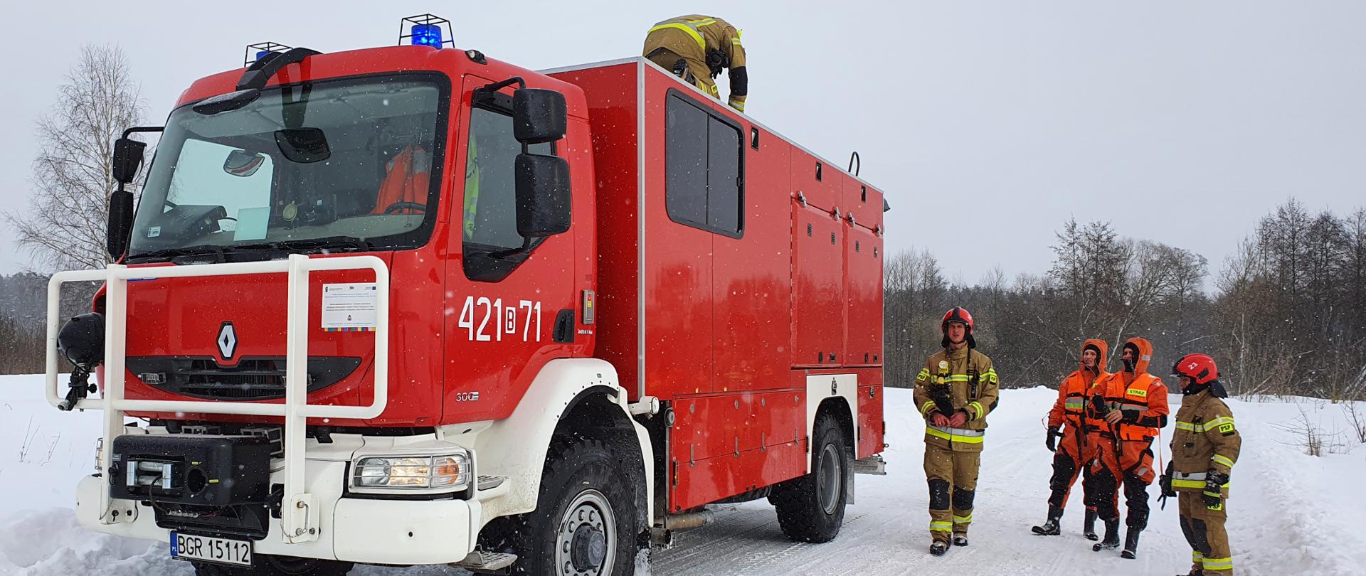 Na zdjęciu samochód ratownictwa wodnego. Obok stoją strażacy PSP w ubraniach typu nomex oraz ubraniach do ratownictwa lodowego.