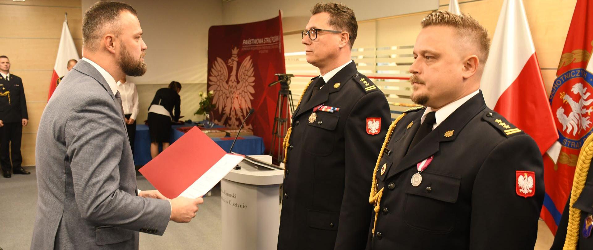 Moment awansowania komendanta miejskiego PSP w Elblągu. Funkcjonariusz stoi na baczność w mundurze wyjściowym.