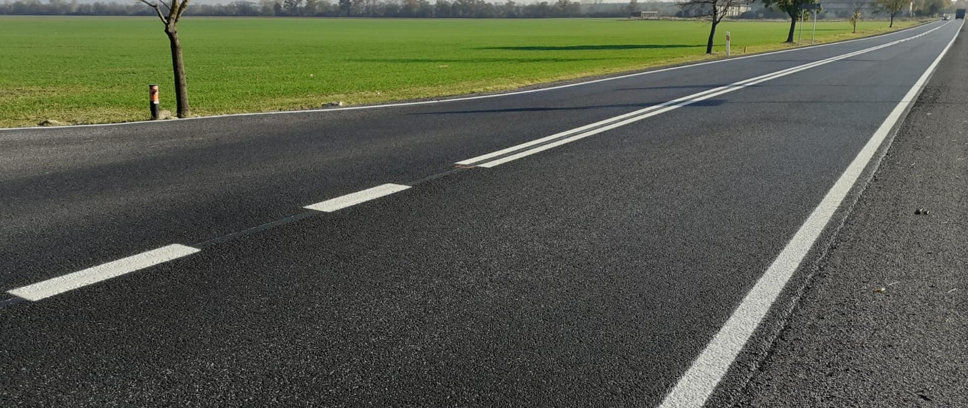 Widok jezdni z wymalowanym oznakowaniem poziomym tj. po lewej i prawej stronie strony linia ciągła, po środku linia przerywana.