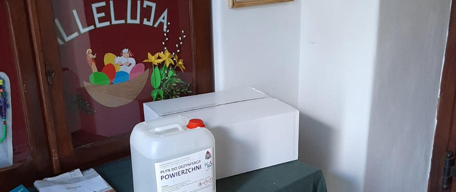 Zdjęcie przedstawia zbiornik środków ochrony indywidualnej na stole jednej z parafii.