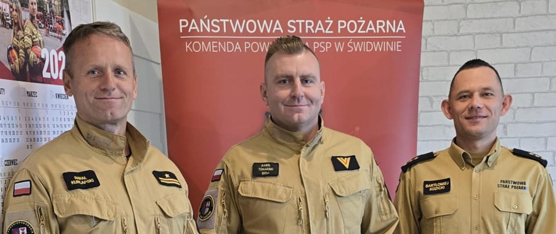 Zdjęcie przedstawia trzech strażaków podczas wręczania nagrody jubileuszowej 20 - lecia pracy i służby