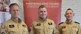 Zdjęcie przedstawia trzech strażaków podczas wręczania nagrody jubileuszowej 20 - lecia pracy i służby