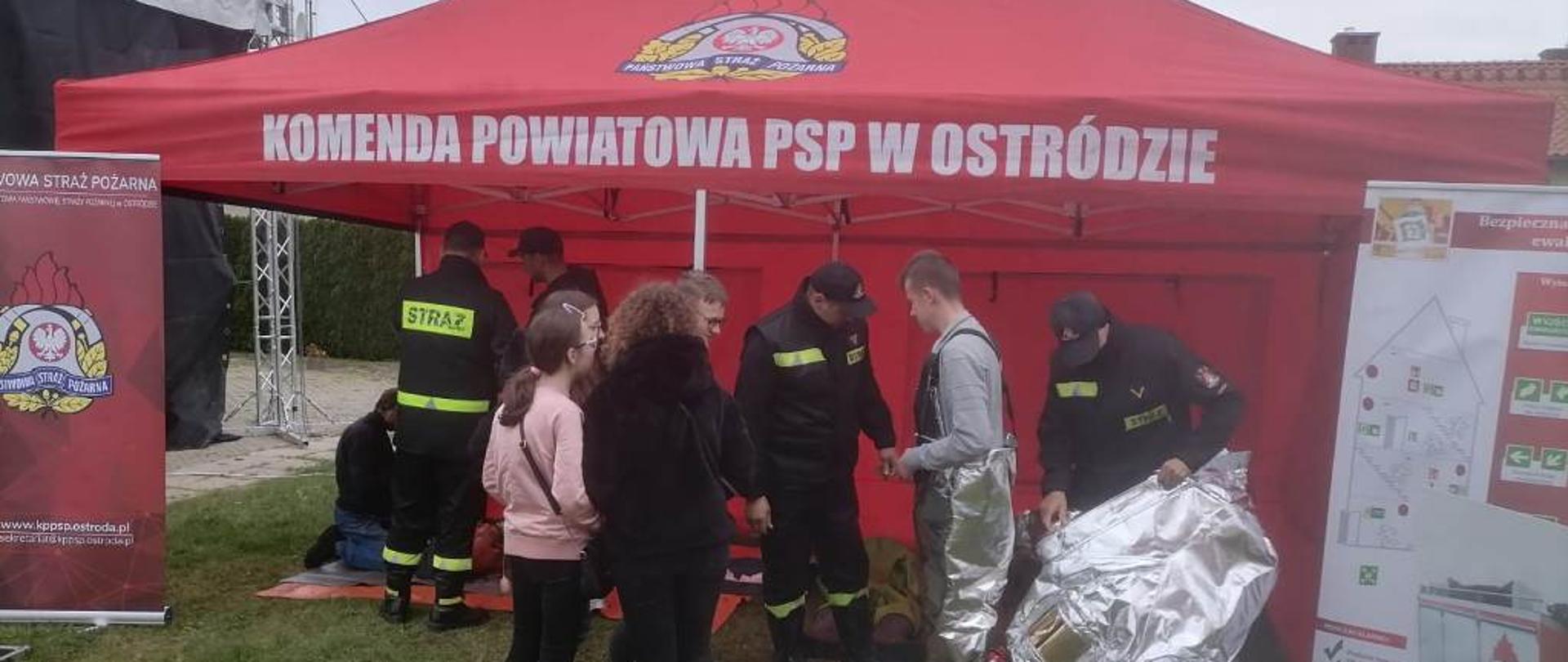 Uczestnicy festynu oglądają i przymierzają strażackie ubrania ochronne