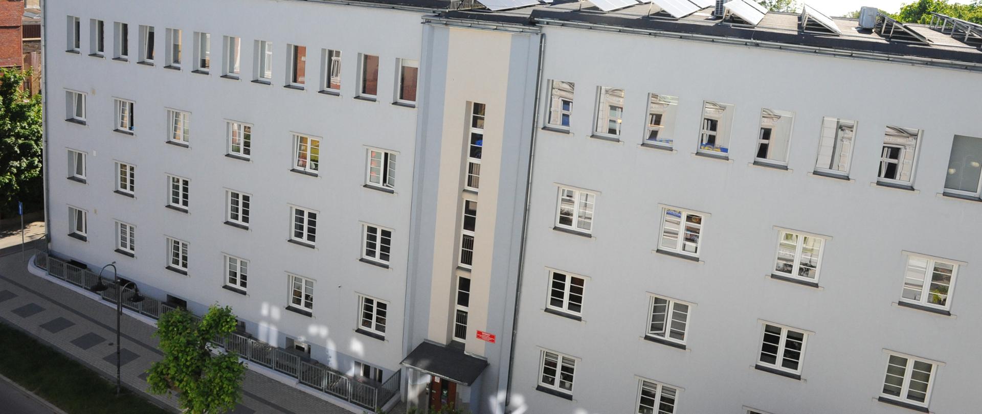 Jasnoszary budynek internatu Zespołu Szkól Centrum Kształcenia Rolniczego w Głubczycach, widok z góry. Widoczne wejście do budynku oraz część ulicy Niepodległości. W oddali widać wieże kościoła i maszt telekomunikacyjny . Na dachu budynku znajduje się instalacja fotowoltaiczna.