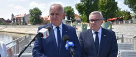 Wojewoda i Prezydent Nowej Soli stoją na przystani, w tle nadbrzeże i rzeka. Przed nimi stoją mikrofony dziennikarzy 