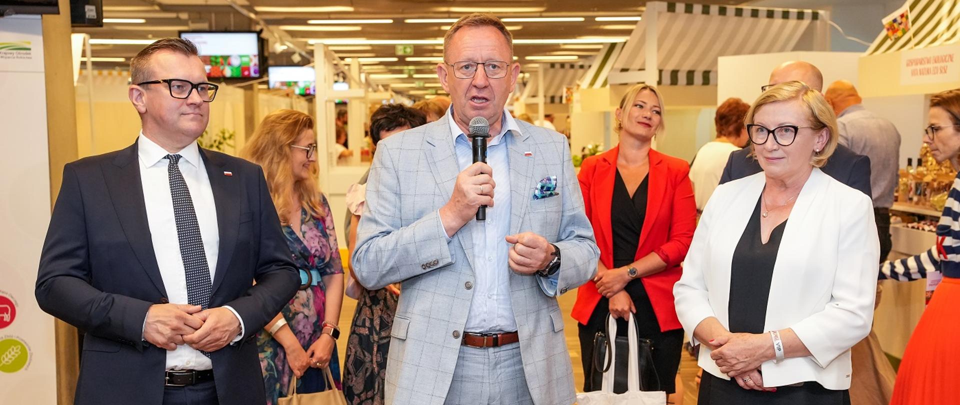 Minister Robert Telus stojący z mikrofonem w prawej dłoni