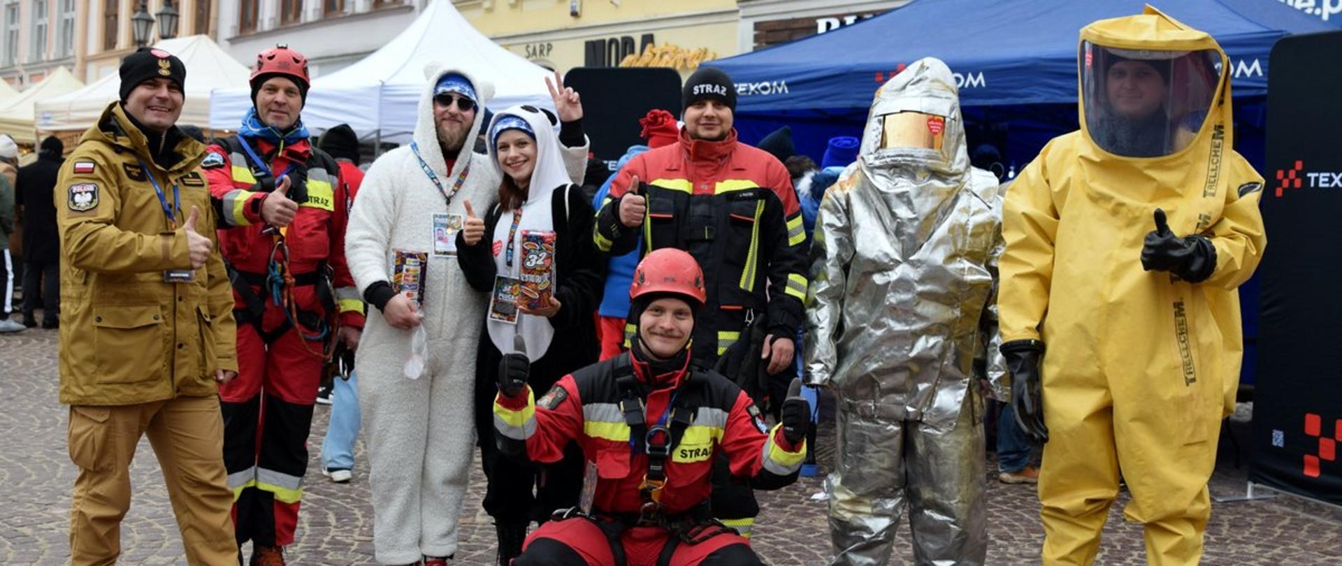Zdjęcie przedstawia strażaków oraz wolontariuszy WOŚP w przebraniach na rynku w Rzeszowie.