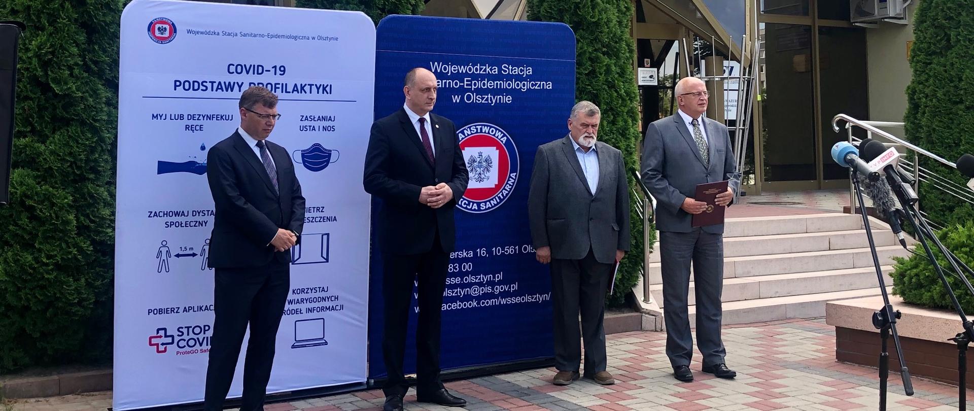 Przed budynkiem Wojewódzkiej Stacji Sanitarno-Epidemiologicznej w Olsztynie stoją w kolejności od strony lewej: Artur Chojecki, wojewoda warmińsko-mazurski, Krzysztof Saczka, Główny Inspektor Sanitarny, profesor Andrzej Zieliński doradca Głównego Inspektora Sanitarnego, Janusz Dzisko, warmińsko-mazurski inspektor sanitarny

