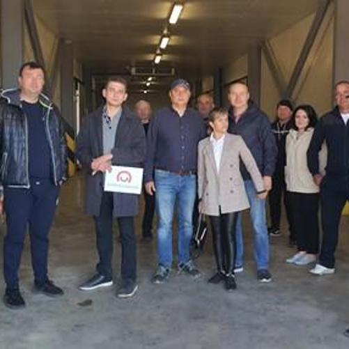 Kilkanaście osób pozuje do zdjęcia w magazynie lub chłodni. Jeden z nich trzyma znak z logo Polskiej pomocy.