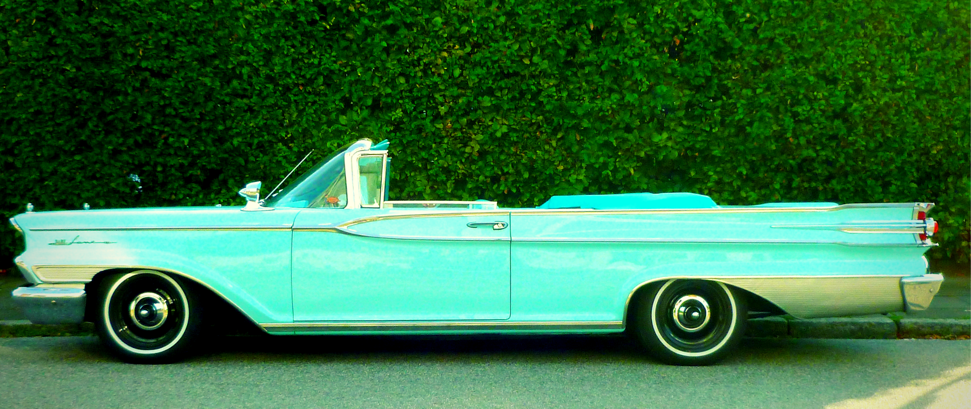 Stojący na ulicy turkusowy zabytkowy kabriolet