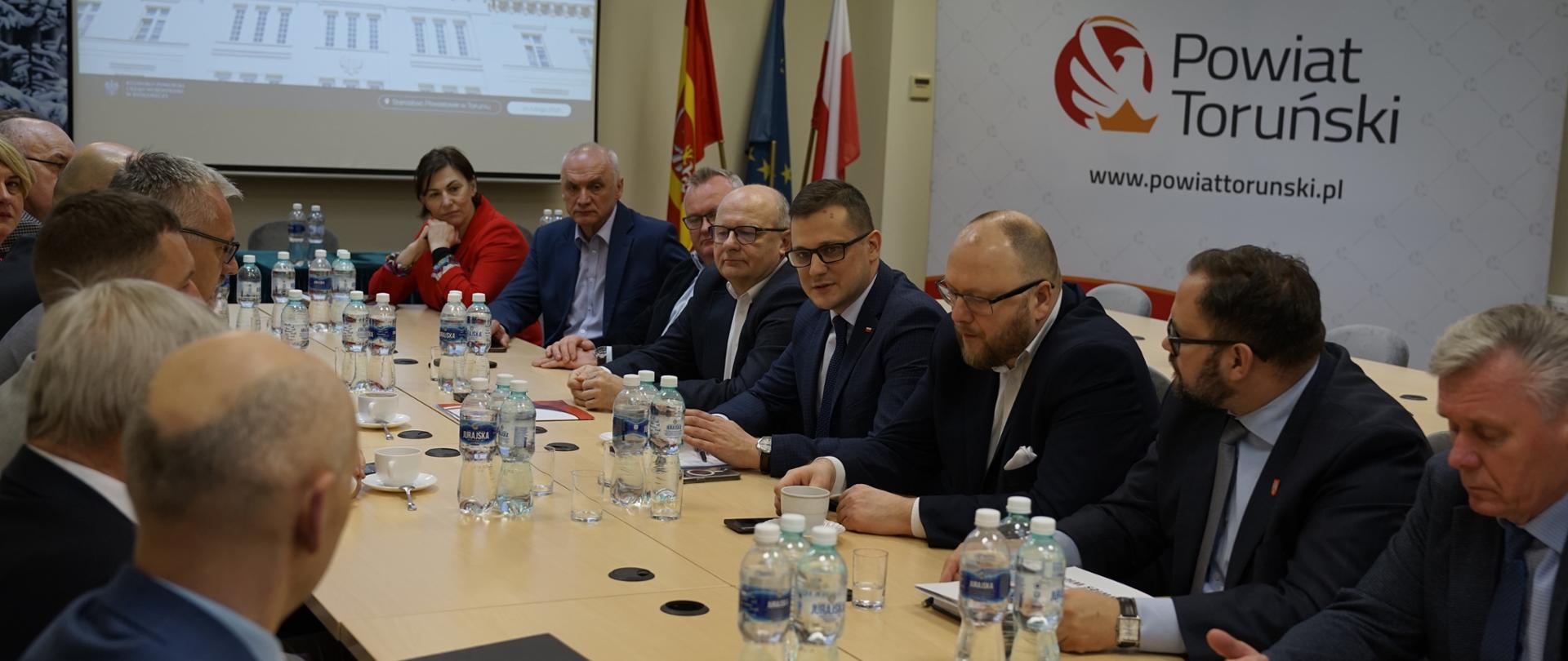 Spotkanie z Samorządowcami w Toruniu. Przy stole siedzi Wojewoda Michał Sztybel wraz ze Starostą Toruńskim Mirosławem Graczykiem oraz innymi uczestnikami spotkania.