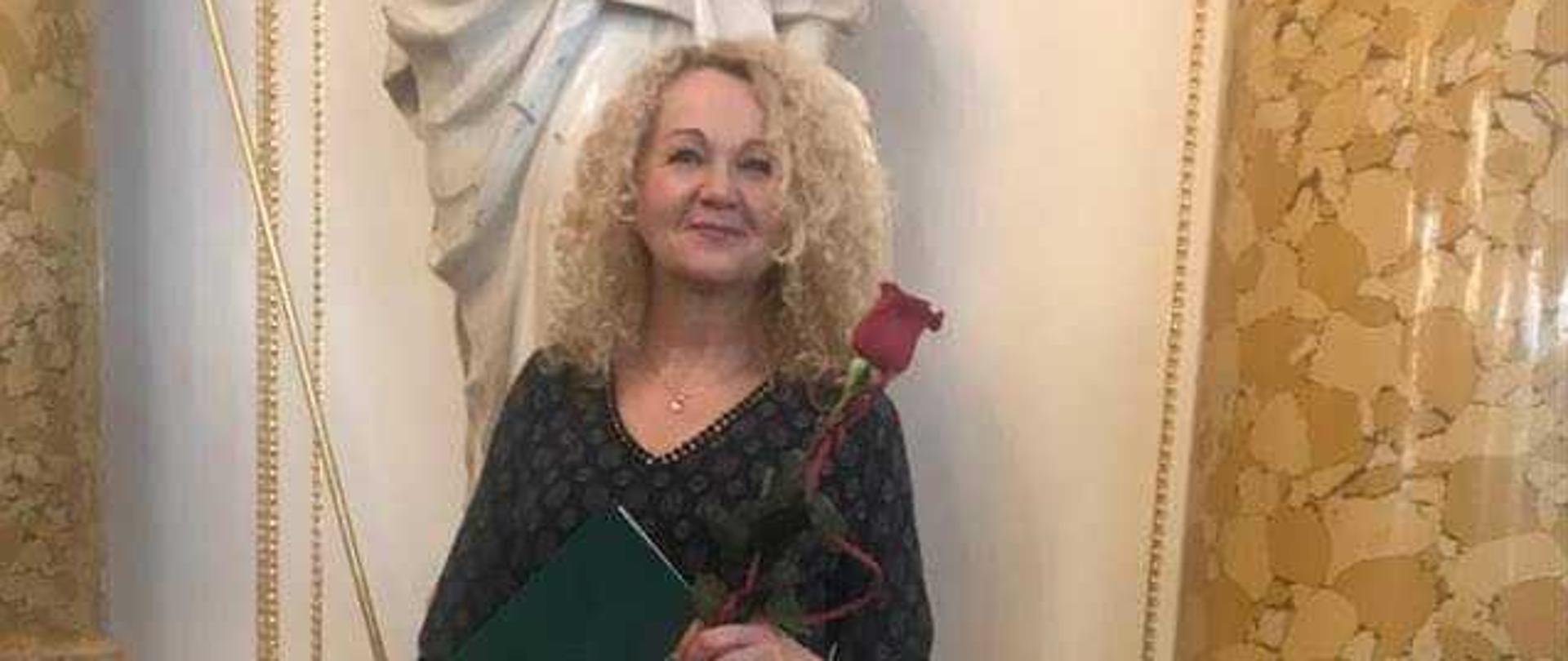 Danuta Gościńska stoi, w ręku trzyma nagrodę i czerwoną różę.