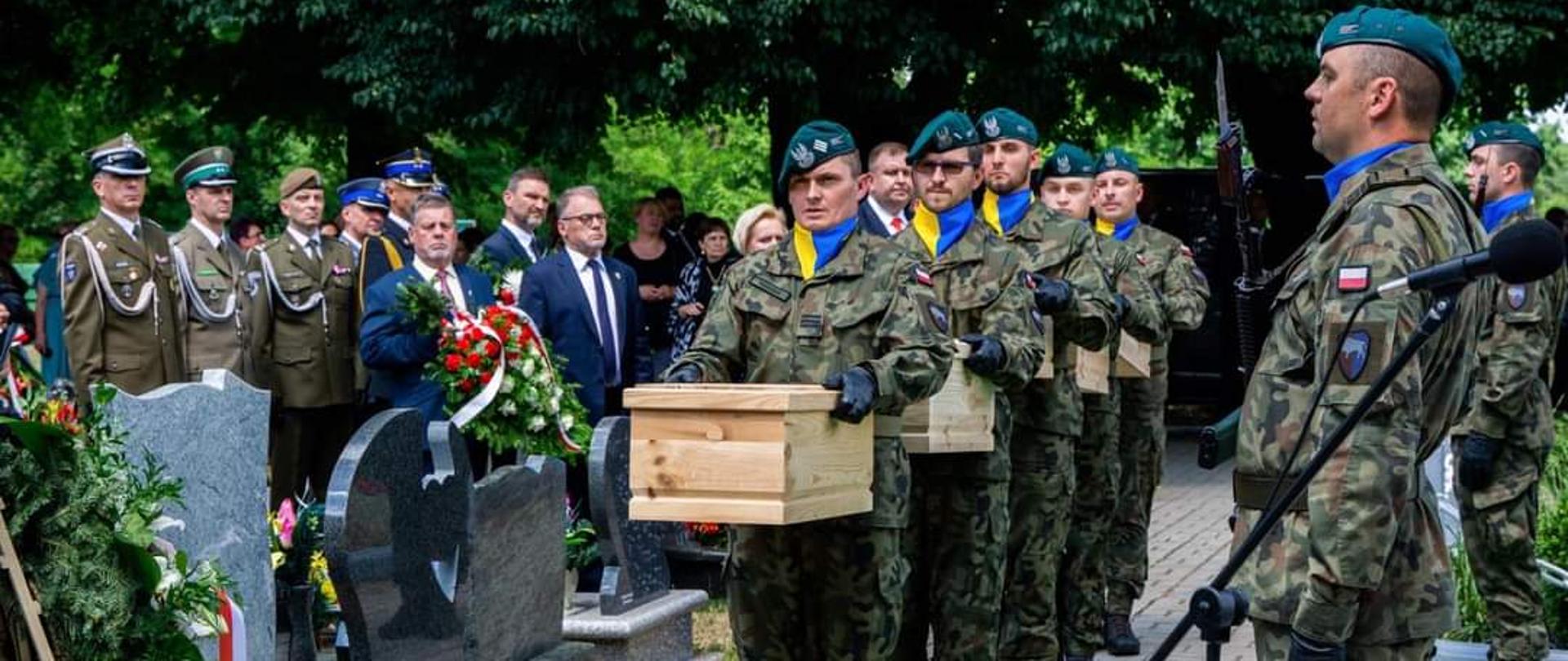 Na zdjęciu ceremonia pogrzebowa Powstańców Śląskich w Kalinowie. W środkowej części kadru stoją żołnierze z 10 BLOG. Trzymają małe, drewniane trumny. Po prawej stronie kadru widać żołnierza, pełniącego wartę honorową. Po lewej stronie kadru uczestnicy pogrzeby Powstańców. Widać również nagrobki na tutejszym cmentarzu. Po lewej stronie kadru na skraju, widać okazały wieniec, wsparty o drewniany stelaż. 