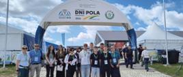 Na zdjęciu widać grupę kilkunastu osób stojących przed głównym wejściem na targi lub wydarzenie branżowe. Nad uczestnikami znajduje się duży biały łuk z napisem „VII Krajowe Dni Pola Szepietowo 2026” oraz logotypami organizatorów i partnerów wydarzenia. Wszyscy mają na szyjach identyfikatory, co sugeruje udział w wycieczce edukacyjnej, szkoleniu lub konferencji.