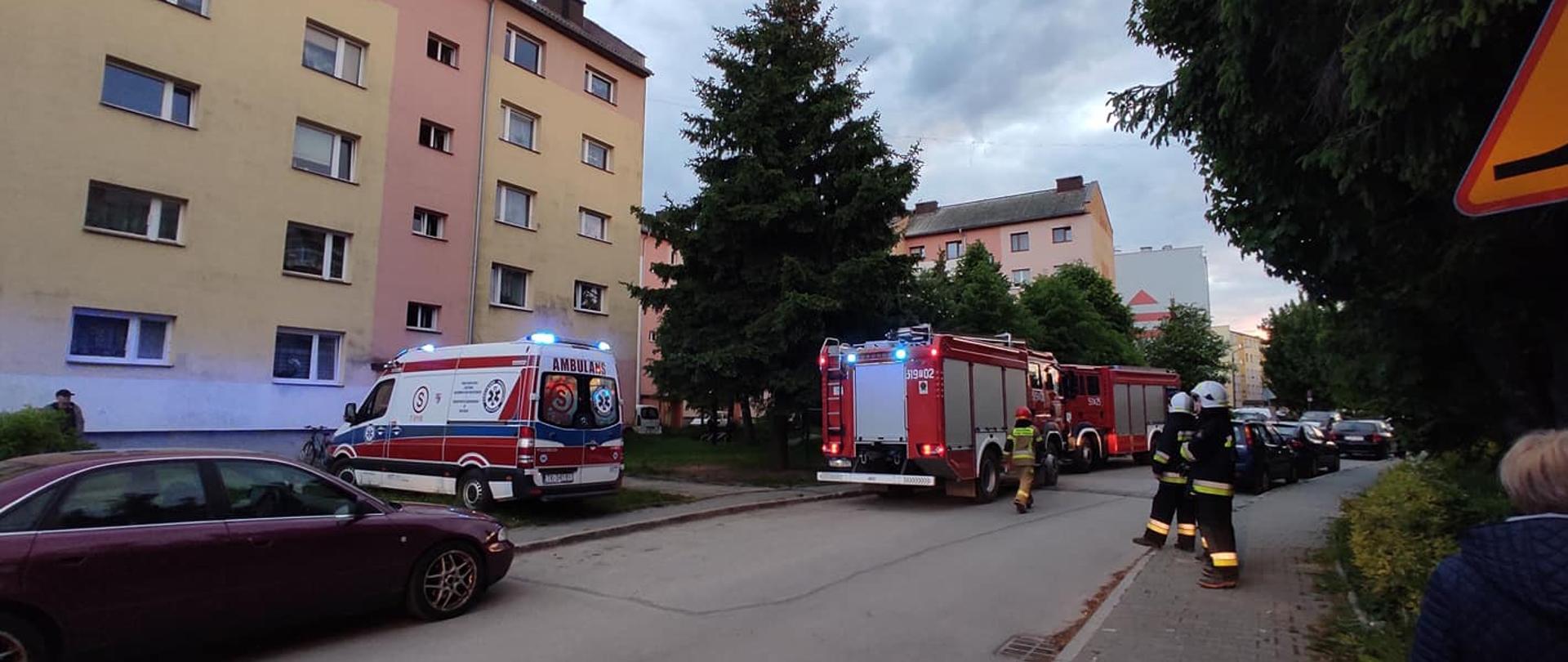 Na zdjęciu budynek wielorodzinny w którym doszło do zadymienia mieszkania oraz klatki schodowej, przed blokiem stoją wozy straży pożarnej oraz karetka pogotowia