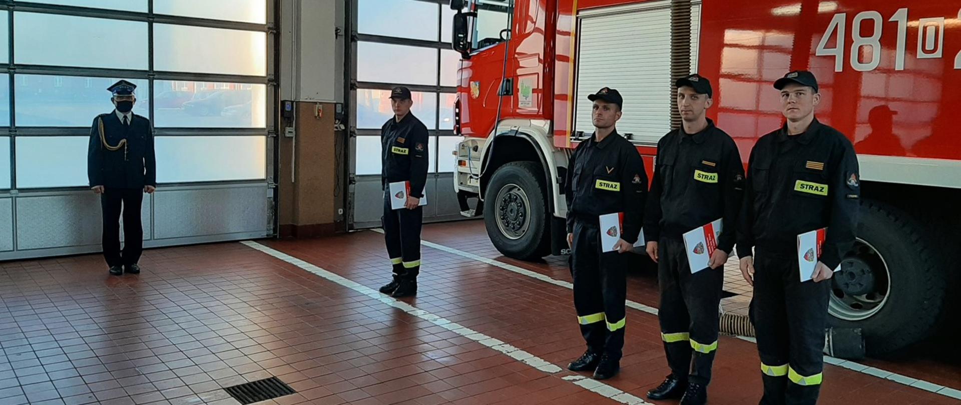 Zdjęcie przedstawia strażaków KP PSP Prudnik, którzy otrzymali listy pochwalne od komendanta. Strażacy stoją w garażu na tle samochodu pożarniczego