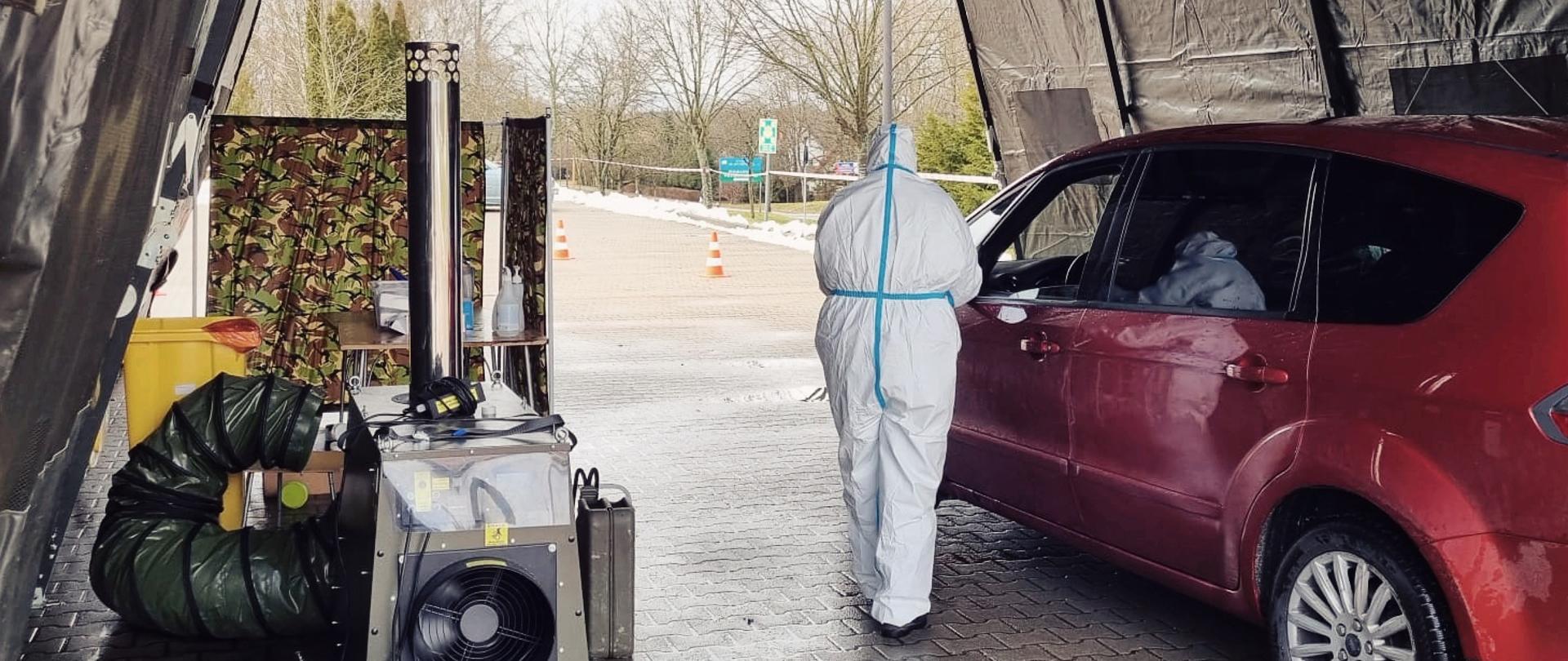 Namiot z człowiekiem ubranym na biało oraz czerwony samochód