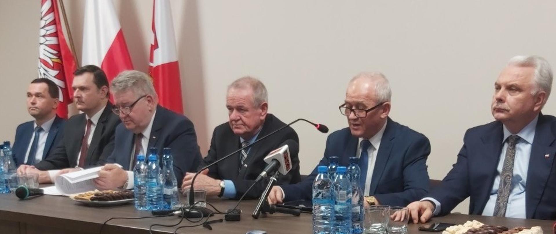 Na zdjęciu stół prezydialny, przy którym siedzi sześciu uczestników konferencji. 