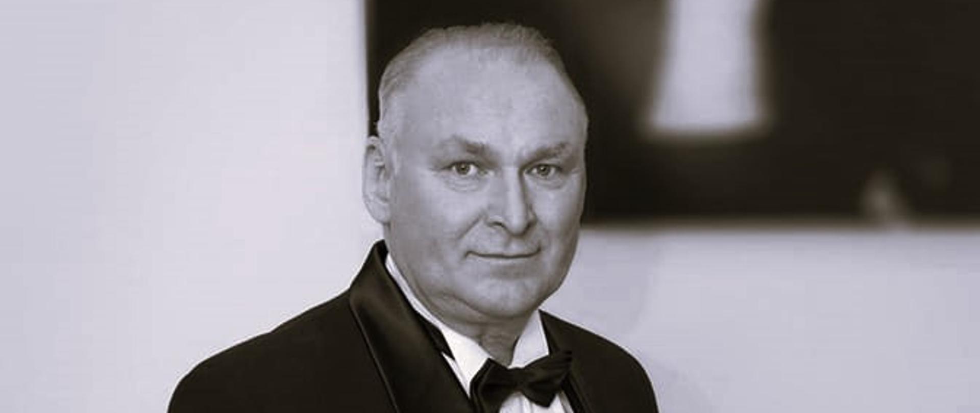 Na zdjęciu czarno-białym wizerunek stojącego bokiem mężczyzny z muchą w garniturze. Stoi obok fragmentu fortepianu. W rękach trzyma klarnet. Twarz mężczyzny skierowana jest na oglądającego. W prawym górnym rogu za mężczyzną nieczytelny fragment obrazu.