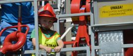 Wspieramy leczenie Gosi. Laureat licytacji "Dnia ze strażakami w Komendzie Powiatowej PSP w Rawiczu" z 3-letnim synem, w koszu podnośnika hydraulicznego. Chłopiec ma na sobie czerwony hełm oraz żółtą kamizelkę odblaskową.