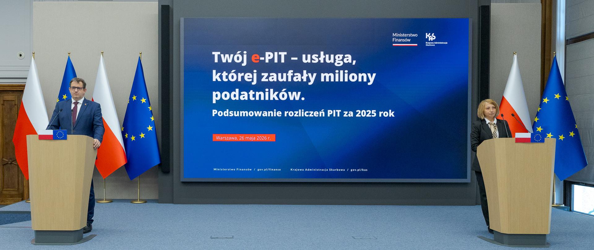 Dwie osoby stoją przy oddzielnych mównicach, a między nimi ekran z napisem „Twój e‑PIT – usługa, której zaufały miliony podatników” oraz informacją o podsumowaniu PIT za 2025 rok.