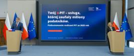 Dwie osoby stoją przy oddzielnych mównicach, a między nimi ekran z napisem „Twój e‑PIT – usługa, której zaufały miliony podatników” oraz informacją o podsumowaniu PIT za 2025 rok.