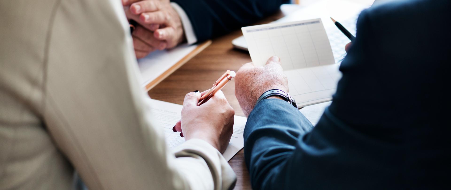 Dłonie trzech osób trzymające długopisy oraz dokumenty na biurku