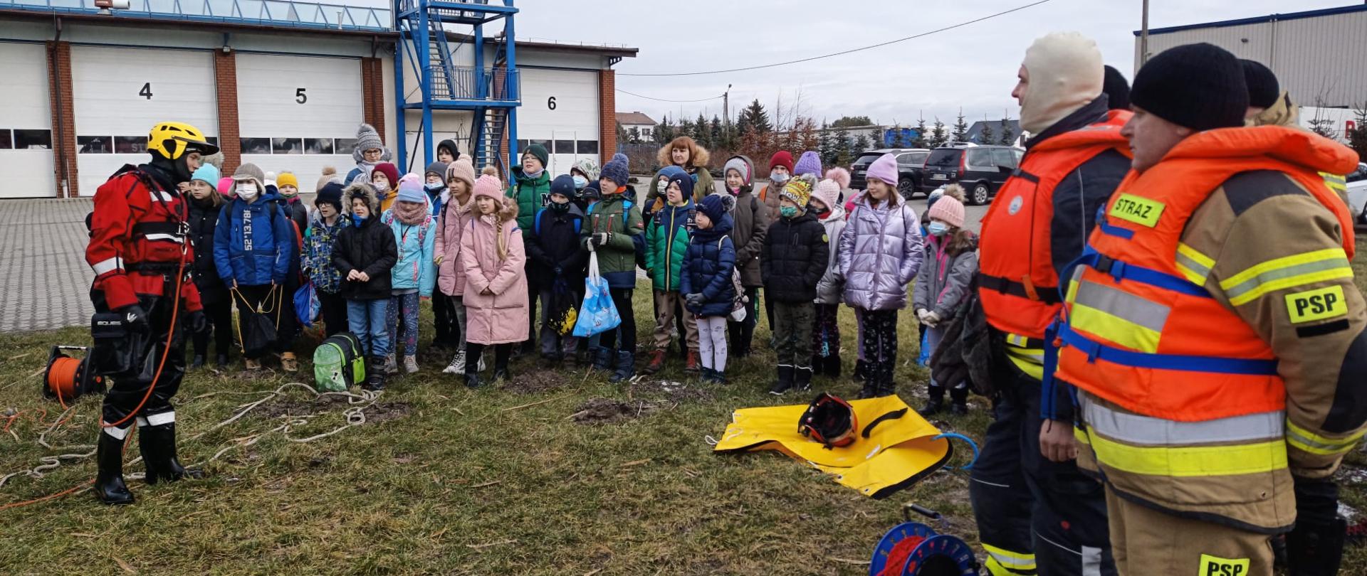 Dzieci słuchają strażaków przebranych w kombinezony