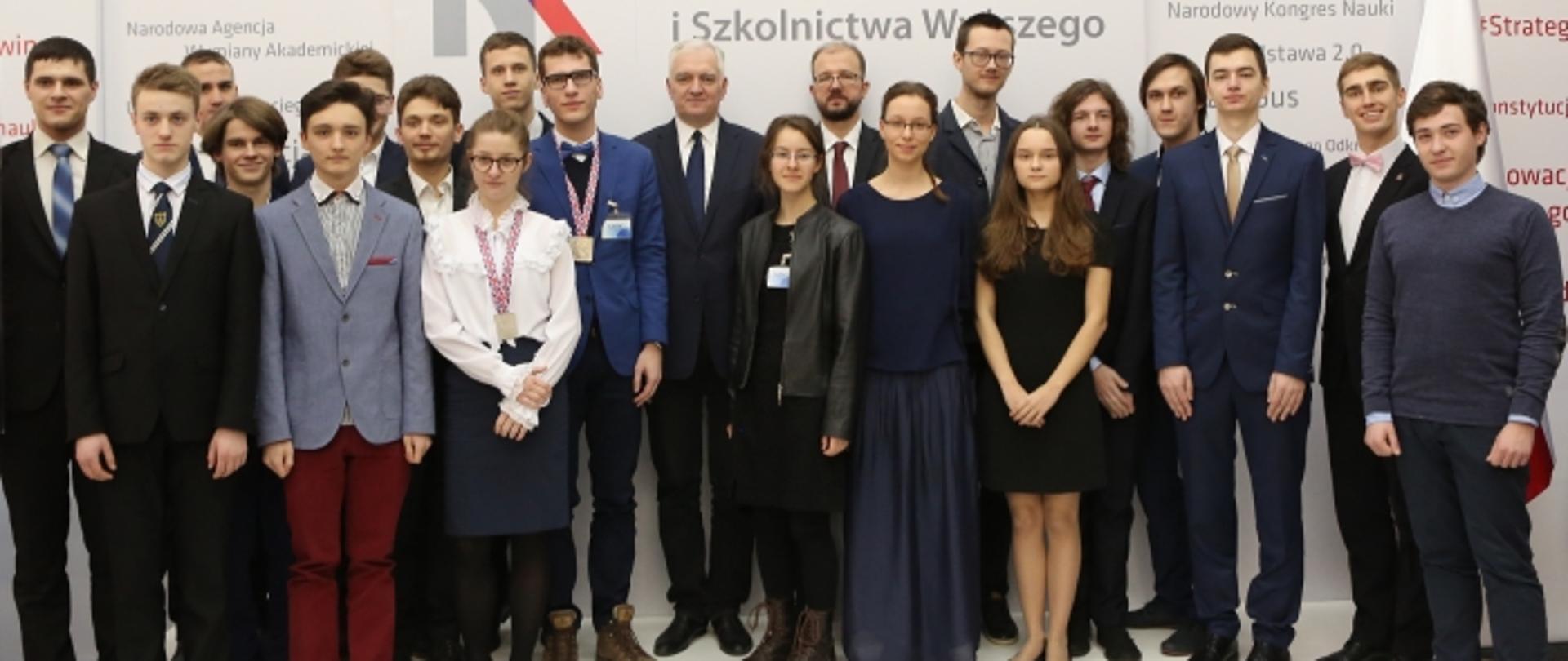 Zdjęcie zbiorowe, na tle scianki w napisem MNiSW stoją medaliści olimpiad