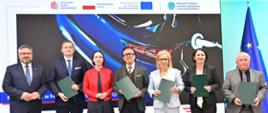 W podpisaniu umowy w dniu 13 maja 2026 r. udział wzięli (na zdjęciu od lewej):
Mirosław Suchoń, Przewodniczący Komisji Infrastruktury, Cyprian Gronkiewicz, Prezes ElectroMobility Poland S.A., Eliza Zeidler, Sekretarz Stanu w Ministerstwie Aktywów Państwowych, Wojciech Balczun, Minister Aktywów Państwowych, Paulina Hennig-Kloska, Minister Klimatu i Środowiska, Dorota Zawadzka-Stępniak, Prezes Zarządu NFOŚiGW, Paweł Augustyn, Zastępca Prezesa Zarządu NFOŚiGW.
