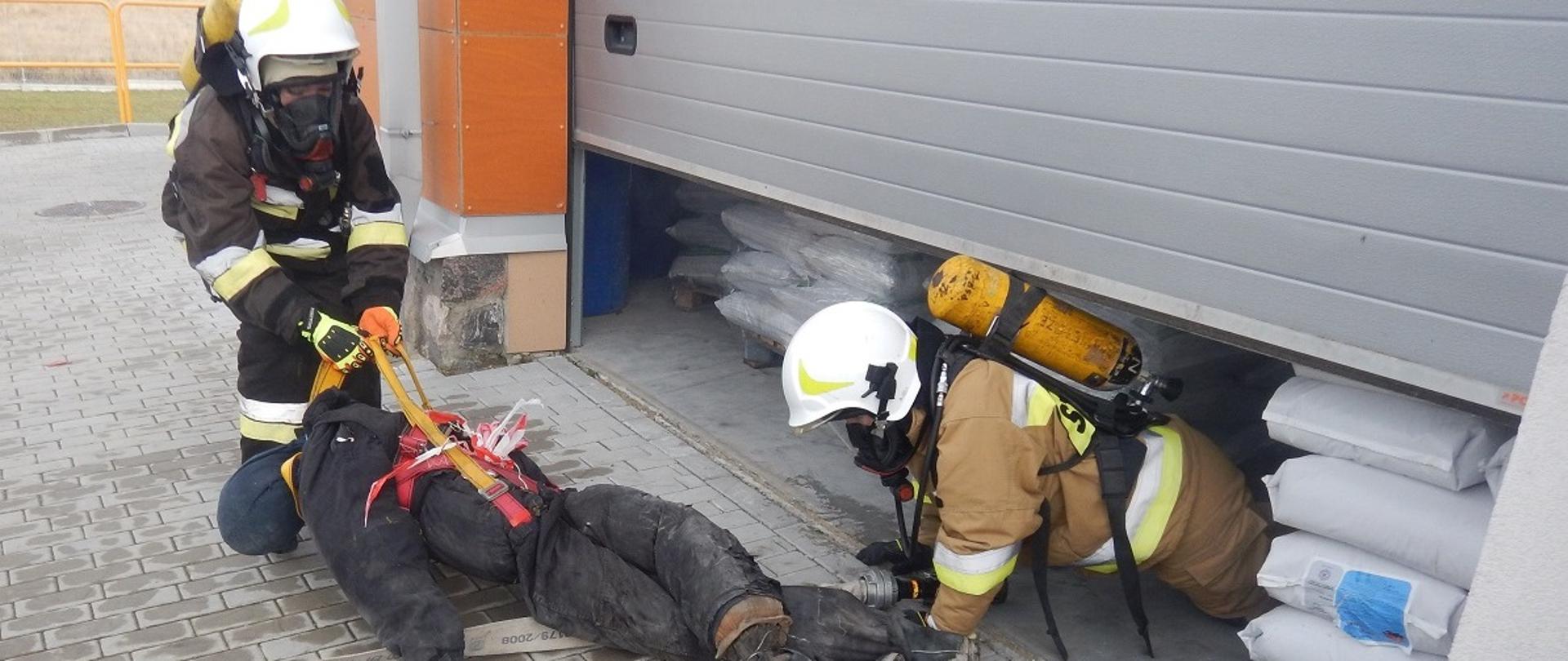 Zdjęcie przedstawia ewakuację osoby poszkodowanej przez dwóch strażaków podczas szkolenia Ochotniczych Straży Pożarnych