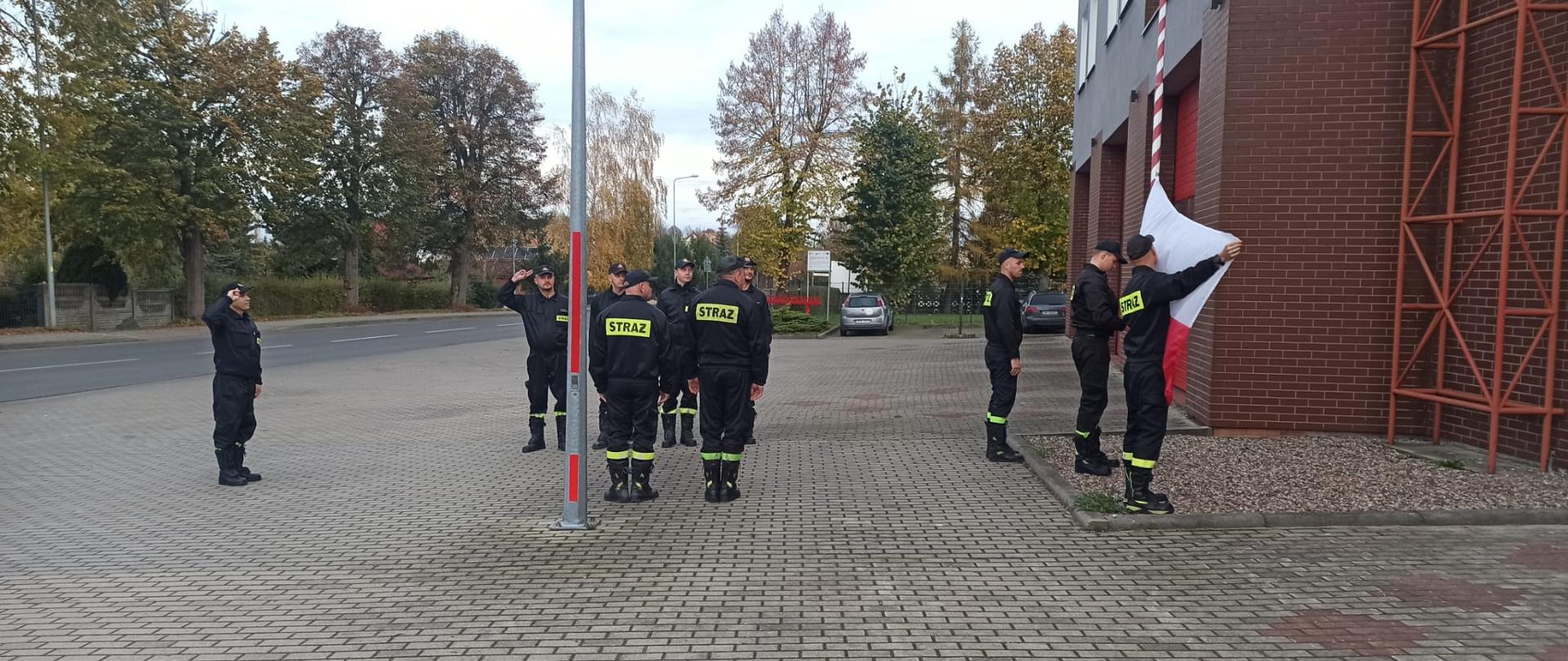 Zdjęcie przedstawia strażaków podczas uroczystego podniesienia flagi państwowej podczas obchodów 11 - go Listopada.