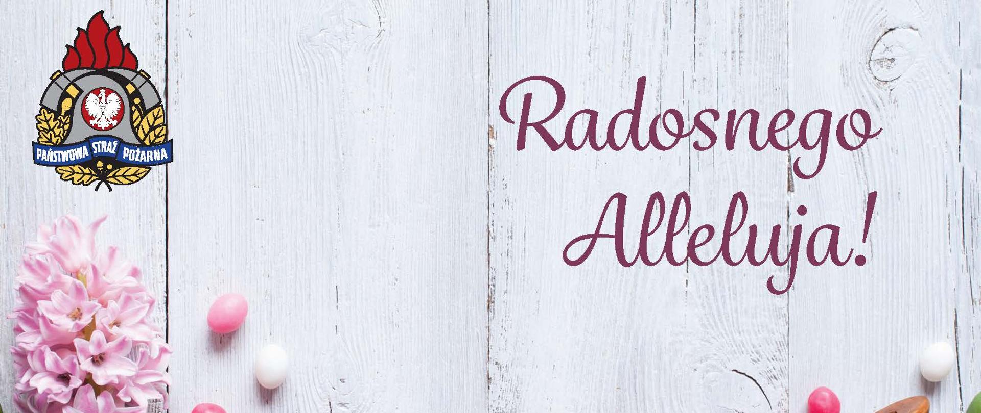 na zdjęciu są pionowo białe deski w lewym górnym rogu logo PSP, po prawej napis Radosnego Alleluja!, na dole kwiaty i pisanki w barwach od różowego do fioletowego