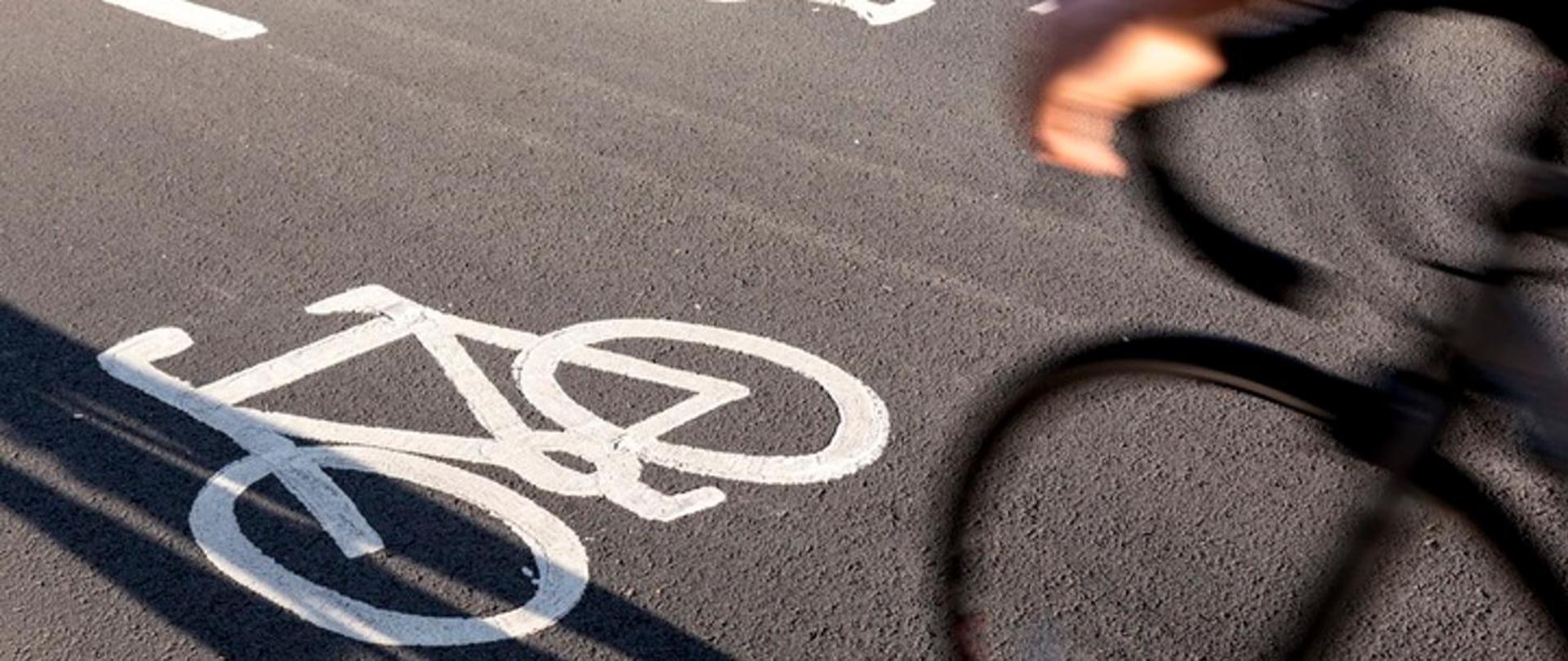 Widoczny namalowany na asfalcie biały rower oraz padający cień roweru 