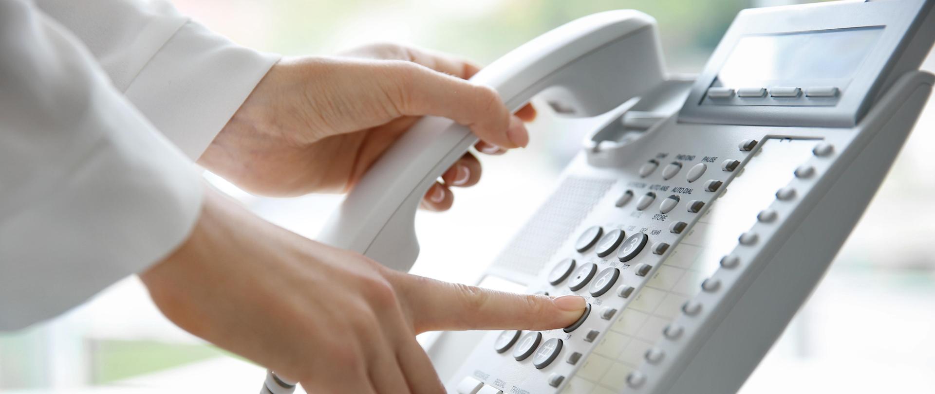 dłoń, kobieta wystukuje numer telefonu na aparacie stacjonarnym