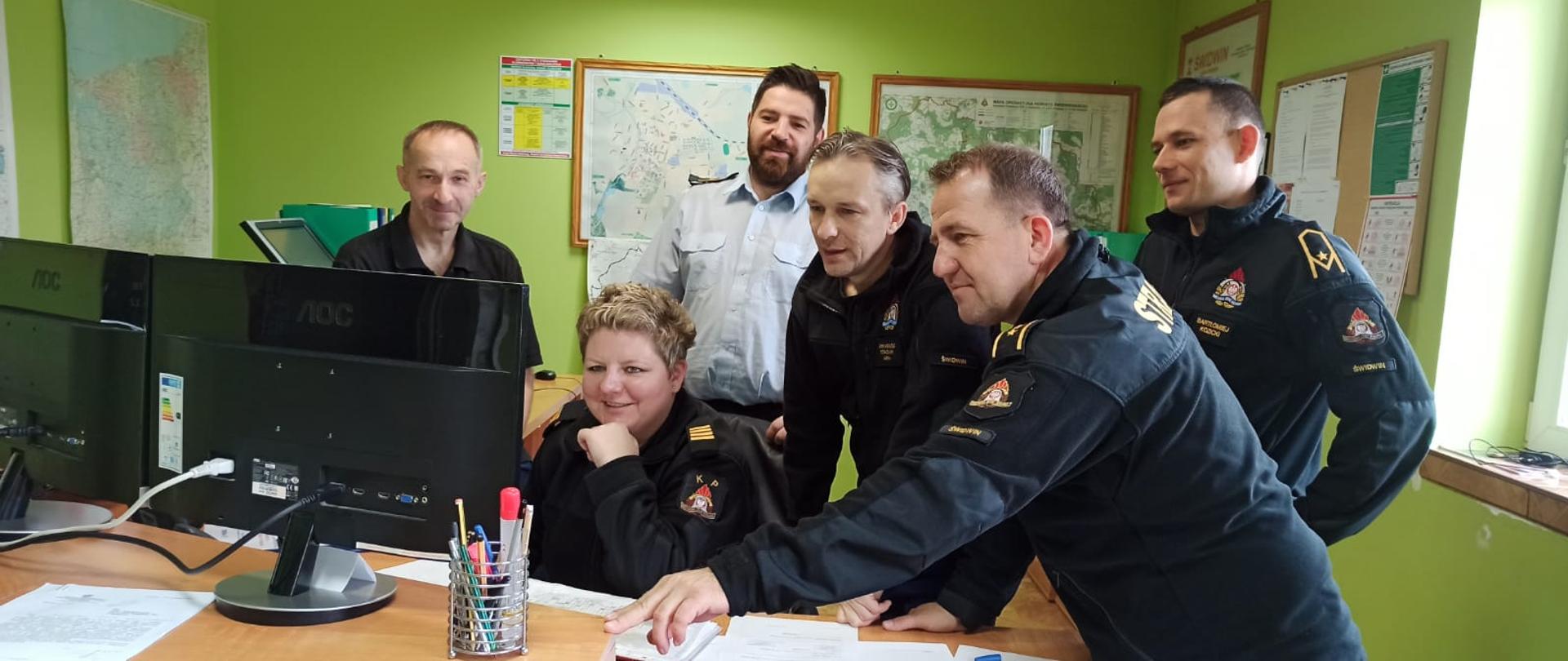 Zdjęcie przedstawia szkolenie Stanowiska Kierowania Komendanta Powiatowego Państwowej Straży Pożarnej w Świdwinie. Dyżurni wpatrują się w komputer. W tle widać mapy oraz segregatory.