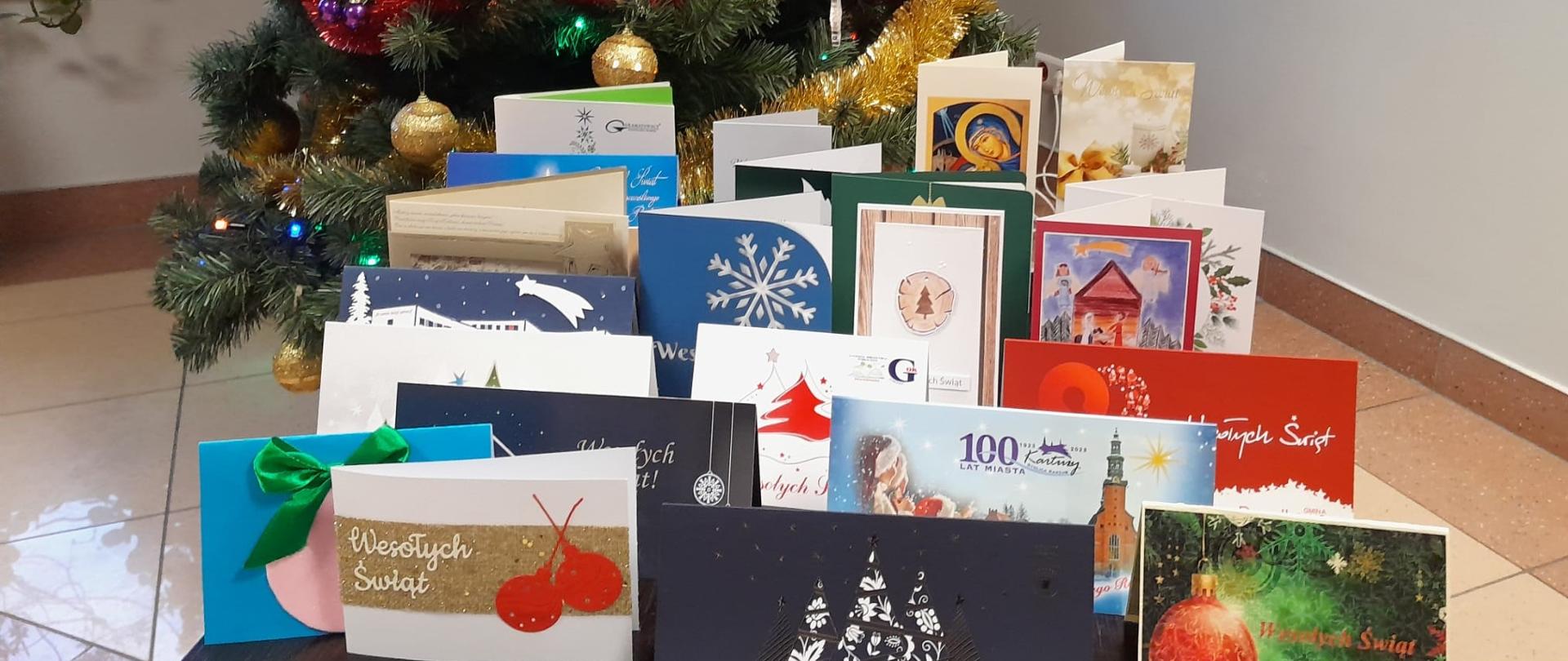Kartki z życzeniami świątecznymi ustawione na stoliku na tle choinki