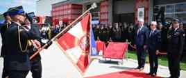 Poczet sztandaru prezentuje nowo nadany sztandar Komendy Powiatowej PSP w Brzozowie. Trzech strażaków w asyście salutuje na czerwonym dywanie. Widoczna jest czerwona strona sztandaru z godłem Polski (Orłem Białym) w wieńcu oraz haftowanym złotym napisem „BOGU I OJCZYŹNIE”. Naprzeciwko stoją oficjele.