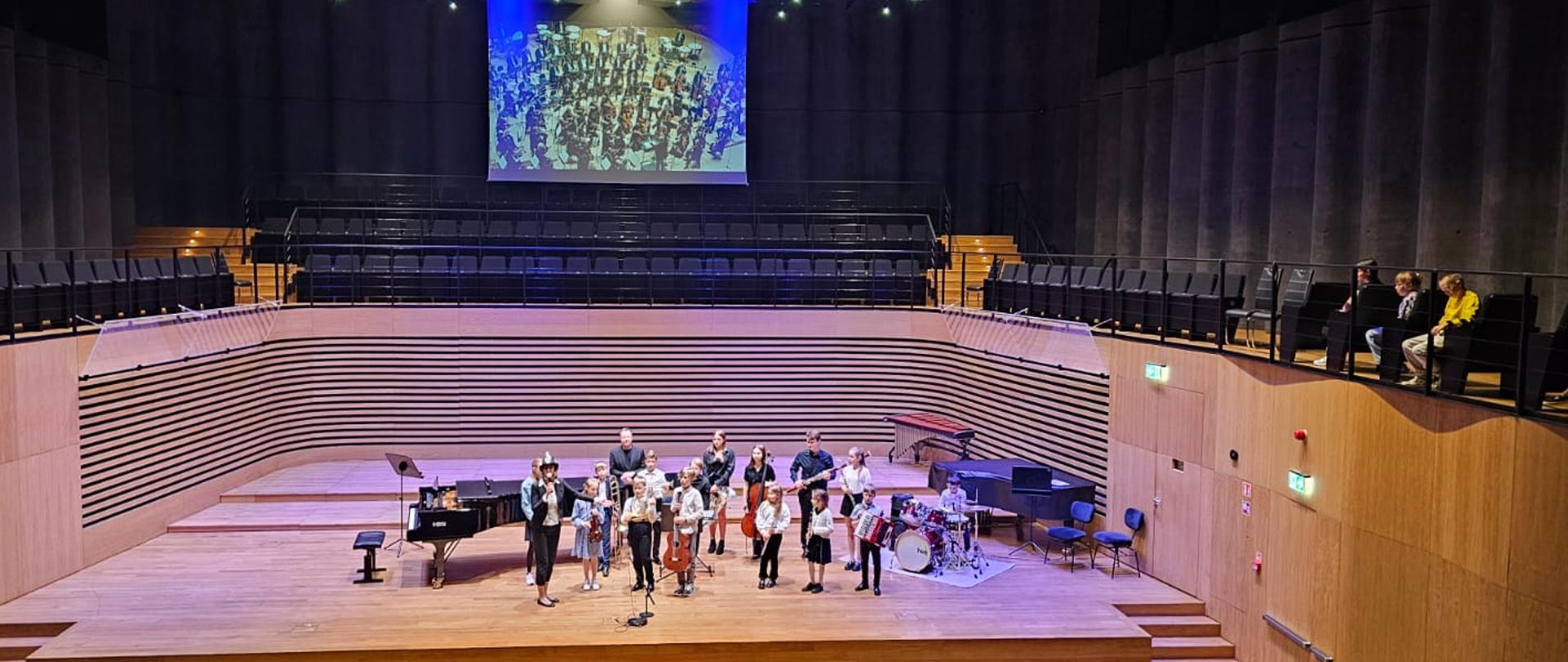 Wszyscy wykonawcy stoją na scenie ze swoimi instrumentami.