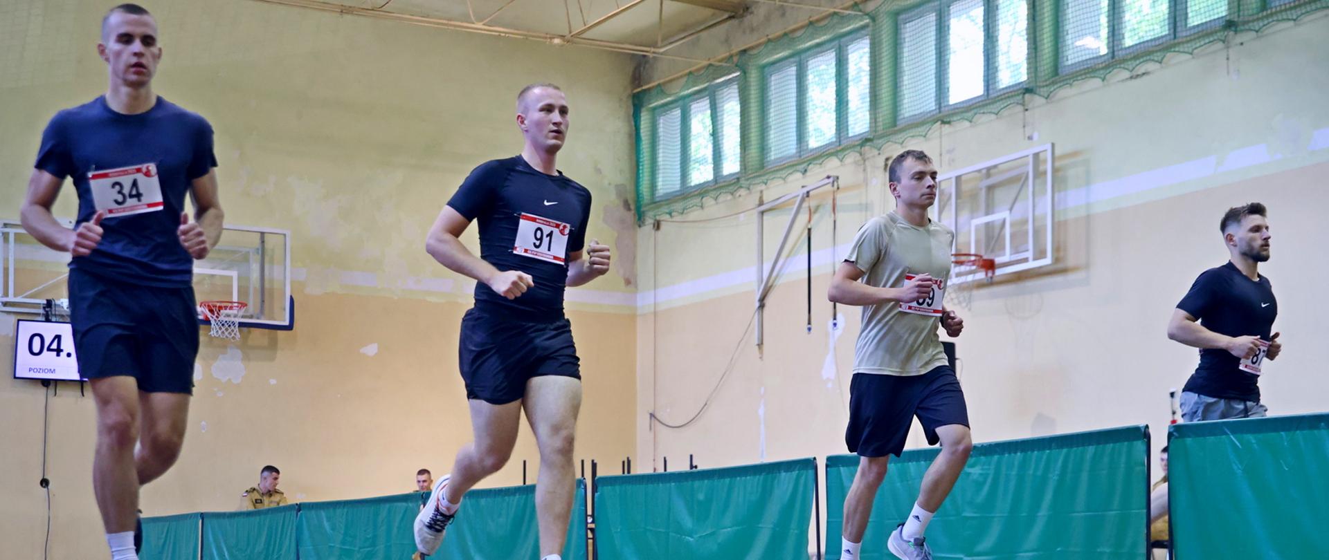 Czterech mężczyzn biegnących po wyznaczonych torach na sali gimnastycznej podczas konkurencji beep-test
