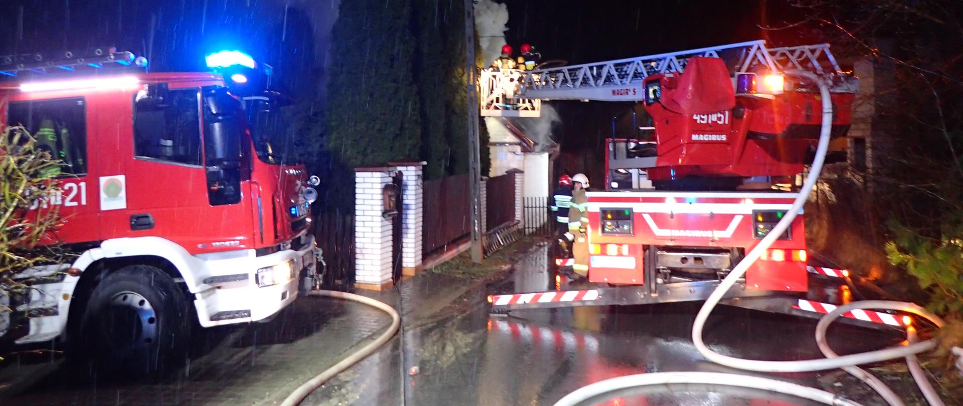 Pojazdy pożarnicze z liniami wężowymi przy pożarze budynku mieszkalnego. Pora nocna