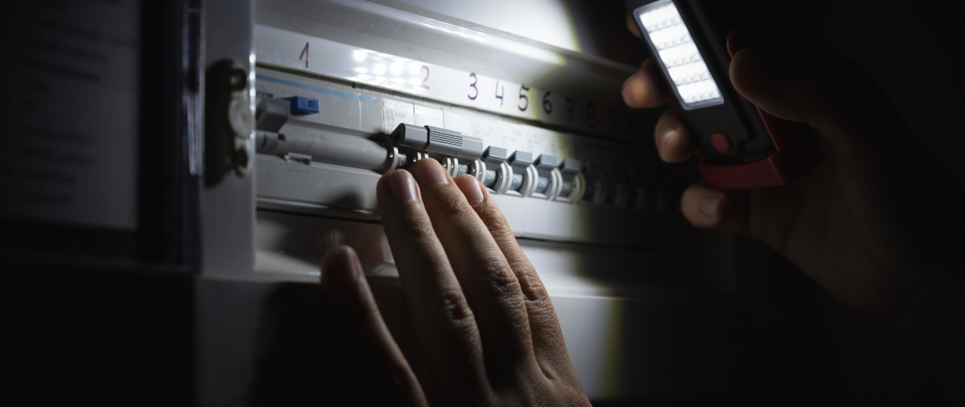 Zdjęcie przedstawiające włączniki prądu oświetlone latarką. Zbliżenie na dłoń, która naciska przyciski. 