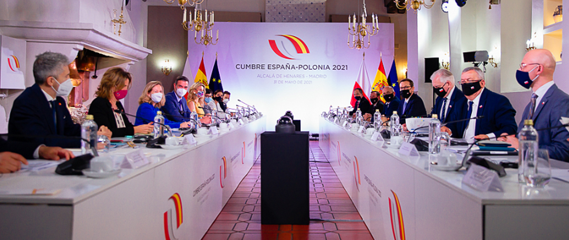 Conference participants sitting on both sides of the table, all wearing masks.