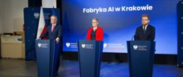 Za trzema mównicami stoją trzy osoby, wiceminister Mrówczyńska w czerwonej marynarce pośrodku między dwoma mężczyznami w czarnych garniturach, za nimi na ścianie wielki ekran z napisem "Fabryka AI w Krakowie" na niebieskim tle.