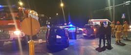 Zdjęcie przedstawia wypadek z udziałem dwóch samochodów osobowych na skrzyżowaniu. Na zdjęciu widać również strażaków, samochód strażacki , radiowóz oraz karetkę pogotowia ratunkowego. 