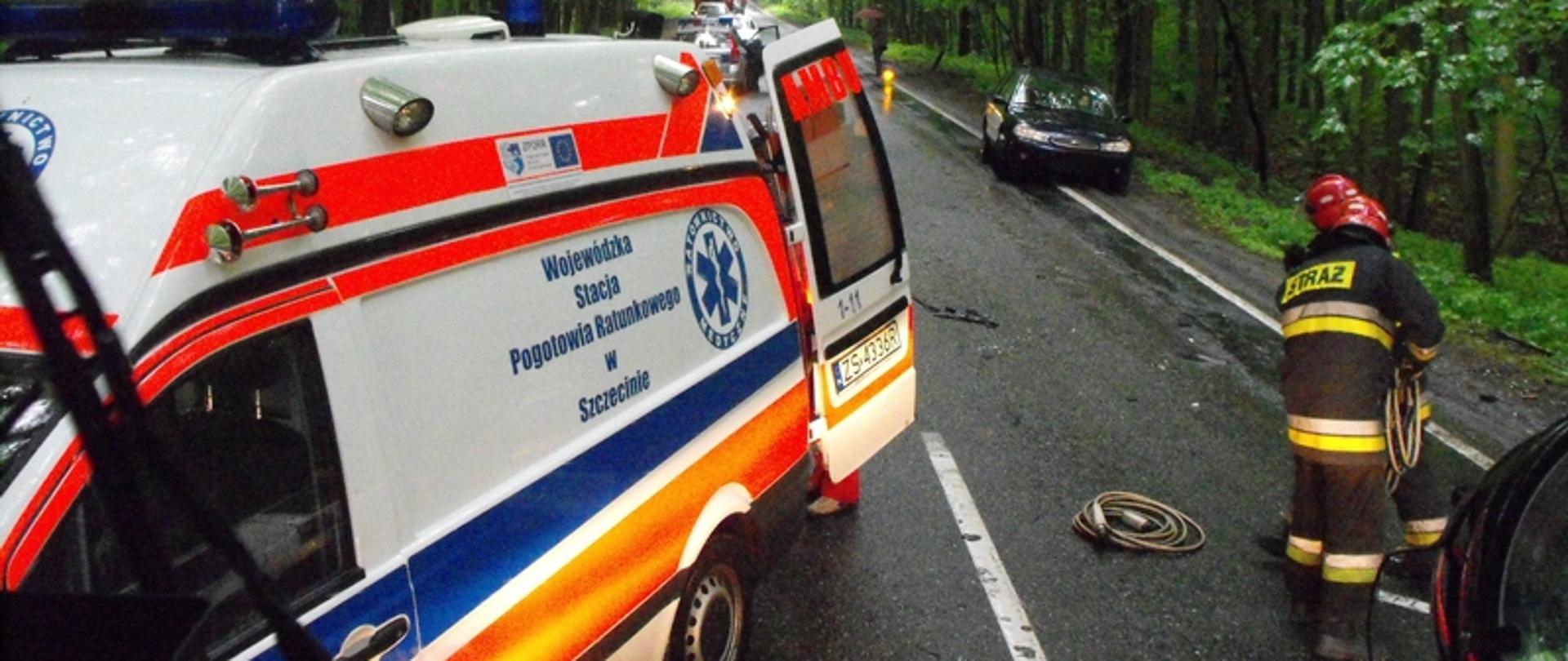 Zdjęcie przedstawia karetkę na drodze w dali samochód osobowy na poboczu