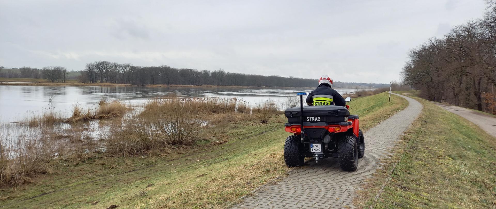 Strażak na quadzie jadący koroną wału wzdłuż koryta rzeki Odry.