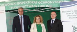 Dwóch mężczyzn i kobieta stoją pod namiotem Wojewódzkiego Inspektoratu Ochrony Roślin i Nasiennictwa w Lublinie. Obok stoi rolap Inspekcji.