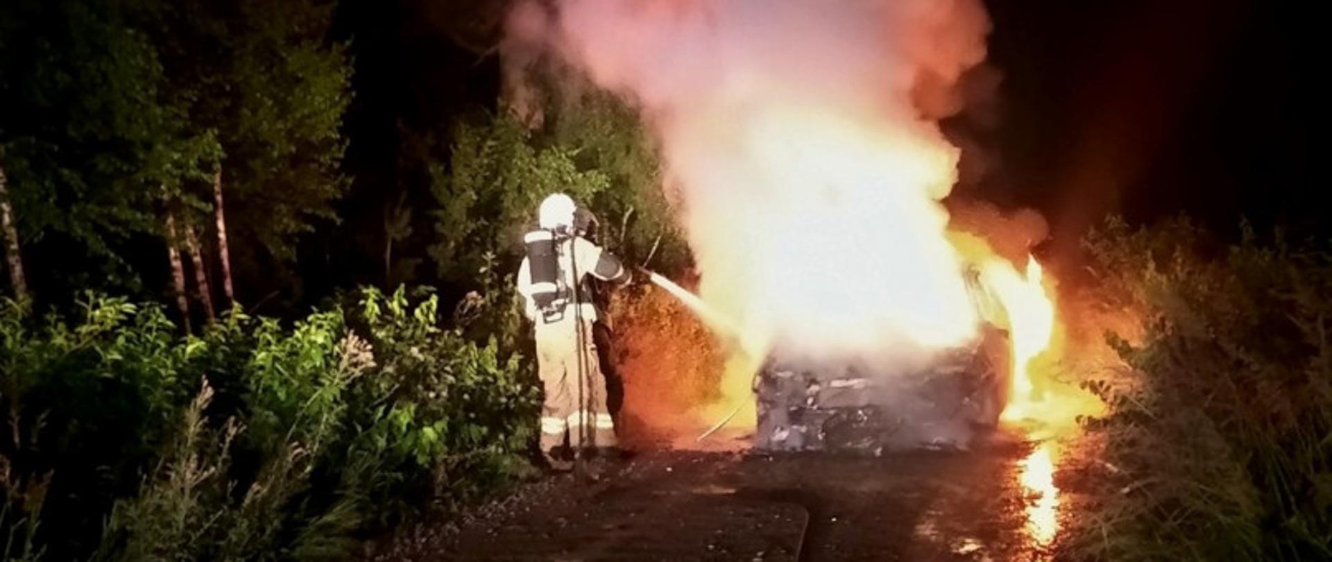 Zdjęcie przedstawia strażaka gaszącego płonący samochód